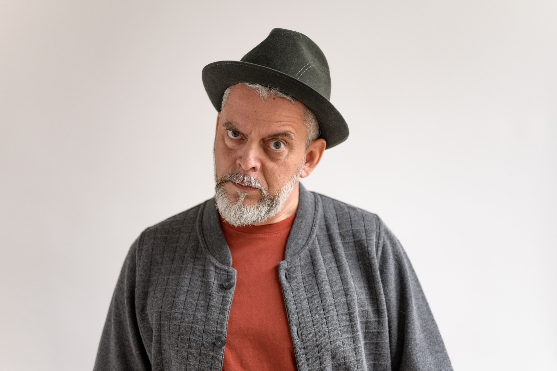 Mature Man in Fedora Hat Shows Skeptical Expression Against Light Wall